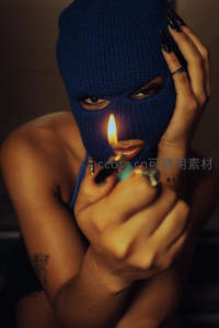 蓝面罩女子持打火机点火，锐利眼神穿透织物，神秘而危险