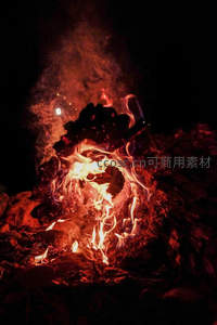 夜幕下熊熊燃烧的篝火，火焰跃动映照炭灰与烟雾升腾