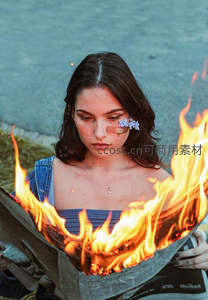 少女手持燃烧报纸，脸上贴花与创可贴，象征伤痛与重生