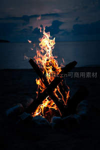 海滩暮色篝火熊熊燃烧，木柴交叉架设，海天交融成剪影