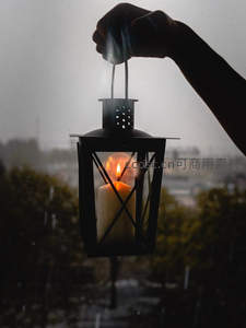 雨中手持铁艺灯笼剪影，烛光穿透窗棂映照朦胧城市