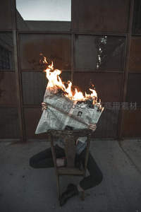 报纸覆面燃烧坐椅上，工业背景隐喻信息过载