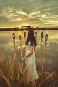 湖畔黄昏，白衣女子持五支火炬背对夕阳，芦苇摇曳如诗