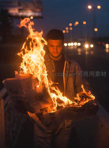 夜色中男子手持燃烧报纸，火焰映照坚毅面庞