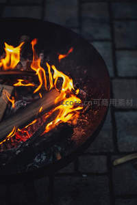 铸铁火盆中木柴燃烧，炭火余烬闪烁，石板地面映衬户外篝火温馨场景