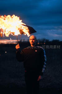 男子暮色中持燃烧雨伞站立旷野，火光撕裂暗蓝天空，超现实街头影像