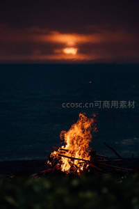 海边暮色下篝火熊熊燃烧，远处云层透出落日余晖映照海面