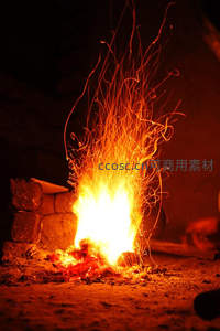 夜幕下篝火迸发炽热火花，石砌火塘映照温暖光影