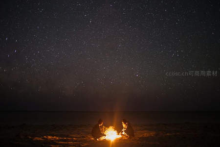 星海之下两人围坐沙滩篝火共度浪漫夜晚