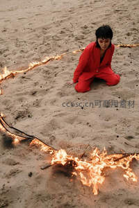 红衣女子跪坐沙地，火焰围成心形，光影交错充满仪式感