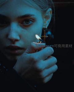 蓝调光影下女子手持打火机，眼神深邃，十字架耳环闪烁微光