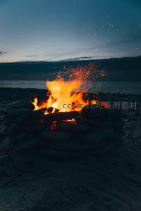 石圈围筑篝火在暮色中跃动，火花四溅映照沙滩夜色