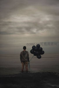阴云密布海边少年手持黑气球伫立浅滩，情绪深沉凝重