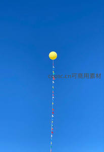 单只黄色气球系彩旗高悬于澄澈蓝天，简约而富有童趣