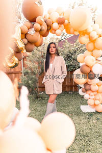 女子立于暖色气球拱门下，庭院派对时尚写真