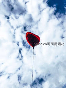 红色心形气球独飞云间：金属质感气球在蓬松白云与深蓝天空中飘荡