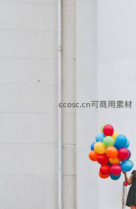 白墙边少女手捧彩虹气球束，简约都市街头童趣瞬间