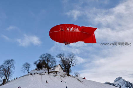 红色Valais飞艇掠过雪山教堂，冬日阿尔卑斯滑雪场全景