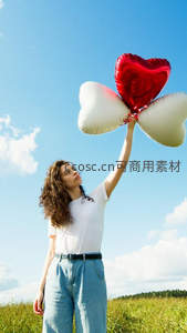 卷发女子仰望蓝天手持红白爱心气球