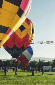 热气球准备升空现场，人群协作牵引，绿野山影相映成趣