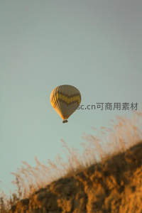 金色夕阳下热气球掠过荒漠草坡，温暖光影勾勒宁静飞行瞬间