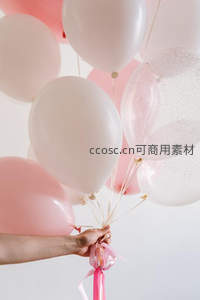 柔光中手握粉白气球束，丝带轻扬，营造温馨浪漫庆典氛围