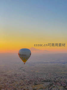 单只热气球掠过城市上空，远山剪影映衬金色黄昏的宁静时刻