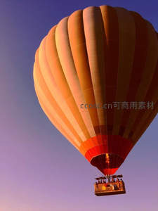 日落时分橙红热气球升空，乘客在篮中仰望渐变紫蓝天空