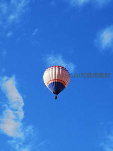 红白蓝条纹热气球悠然升空，湛蓝天空点缀朵朵白云
