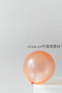 单颗蜜桃色气球静置于白色立方体上，留白构图极简风