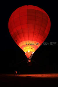 夜幕下炽热红焰热气球升空，地面人影仰望梦幻光影