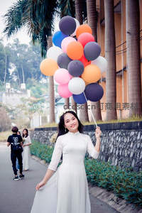 越南奥黛少女手持彩色气球束，棕榈树下微笑漫步，街头人文纪实风