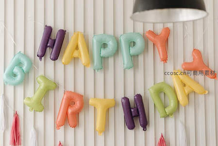 彩色字母气球拼出HAPPY BIRTHDAY，背景为竖条纹墙面
