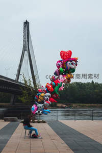 河畔现代斜拉桥下，摊贩手持卡通气球束，城市休闲一景
