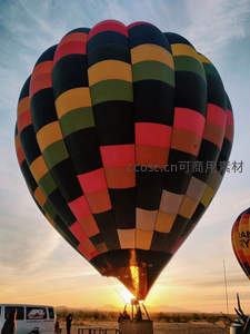 多彩方格热气球日落时分升空，火焰喷涌映照沙漠剪影