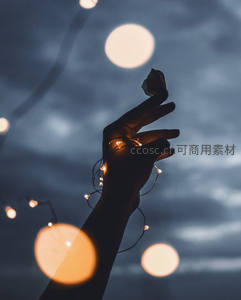 剪影手掌轻托发光灯串，背景虚化光斑如星月点缀暮色天空