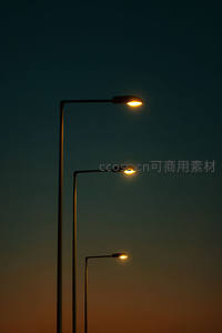 黄昏时分三盏路灯剪影，暖光映衬渐变暮色天空