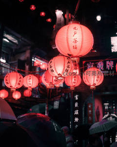 雨夜街巷灯笼映照湿漉青石板，行人撑伞穿行，烟火气十足