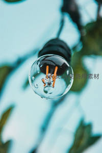 特写水珠覆盖的LED灯泡，橙色灯丝在青蓝背景中透出科技与自然交融之美