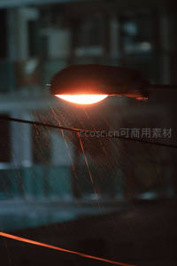 雨夜街灯特写，橙黄光晕映照斜飞雨丝，背景虚化朦胧