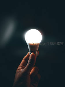 手握发光LED灯泡特写，黑暗中明亮光源象征创新与希望