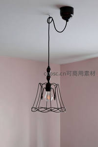 黑色铁艺笼式吊灯悬于粉墙角落，复古工业风室内照明特写