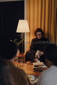 暖光阅读角：卷发男子手捧书本，落地灯映照沉静思考时光