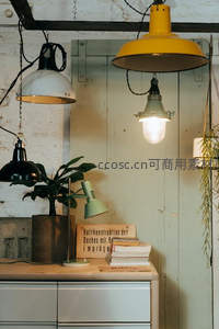 工业风工作台场景：黄绿黑吊灯、绿植、德文标牌与堆叠书籍营造复古文艺氛围