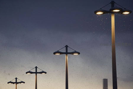 雨夜城市路灯群亮起，水珠飞溅中现代灯杆剪影映衬渐变暮色天幕