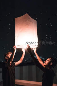 夜空下两人合力放飞孔明灯，星光点点映衬温暖光晕