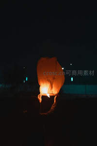 夜空下双手托举点燃的孔明灯，微光映照剪影轮廓