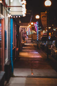 夜市街道霓虹闪烁，彩灯串装饰人行道，车辆停靠，氛围温馨浪漫