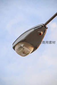 仰拍老旧路灯特写，灰白灯罩与淡蓝天空形成对比
