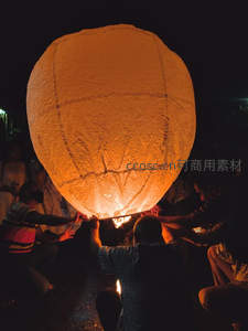 夜幕下众人合力点燃大型孔明灯，暖光映照纸面纹理，传统祈福仪式温馨动人